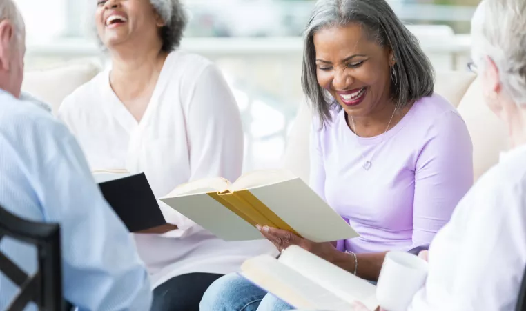 Group of older adults sitting and laughing while reading books. 