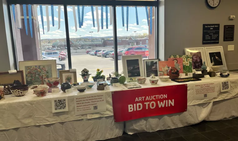 A number of art pieces are sitting on a table with a red banner that reads "Art Auction Bid to Win"