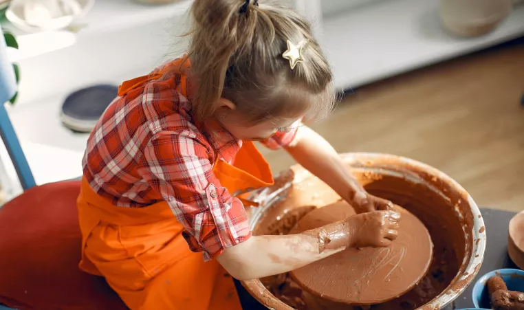 Young child sits at a pottery wheel working with clay.