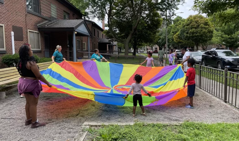 Y staff, kids, and families playing with a colorful parachute