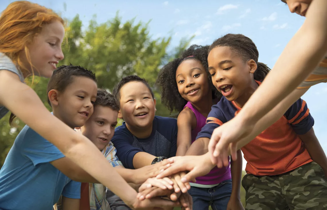 A group of kids putting their hands together for a cheer. 