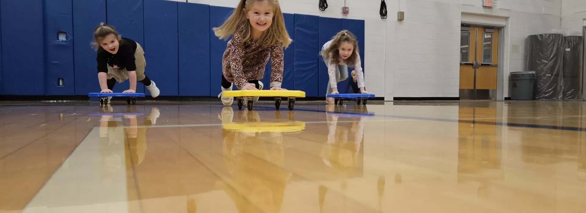 Group of UPK kids use scoot boards in the gym